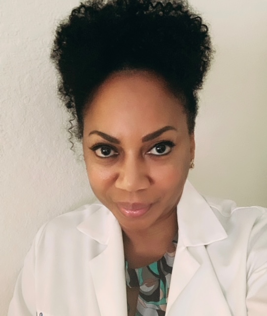 francine Woman in a white lab coat smiling at the camera, standing against a plain light-colored wall.