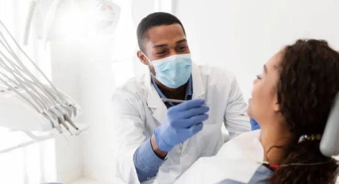 ds-1 A dentist wearing a mask examines a patient in a dental chair, holding dental instruments.