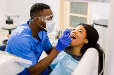 ezgif.com-gif-maker A dentist examines a patient's teeth as she sits in a dental chair, both wearing protective gear.