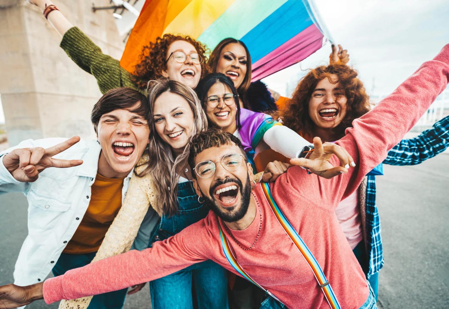 lgbt-friendly-img A joyful group of diverse friends pose together, smiling and holding a rainbow pride flag outdoors.