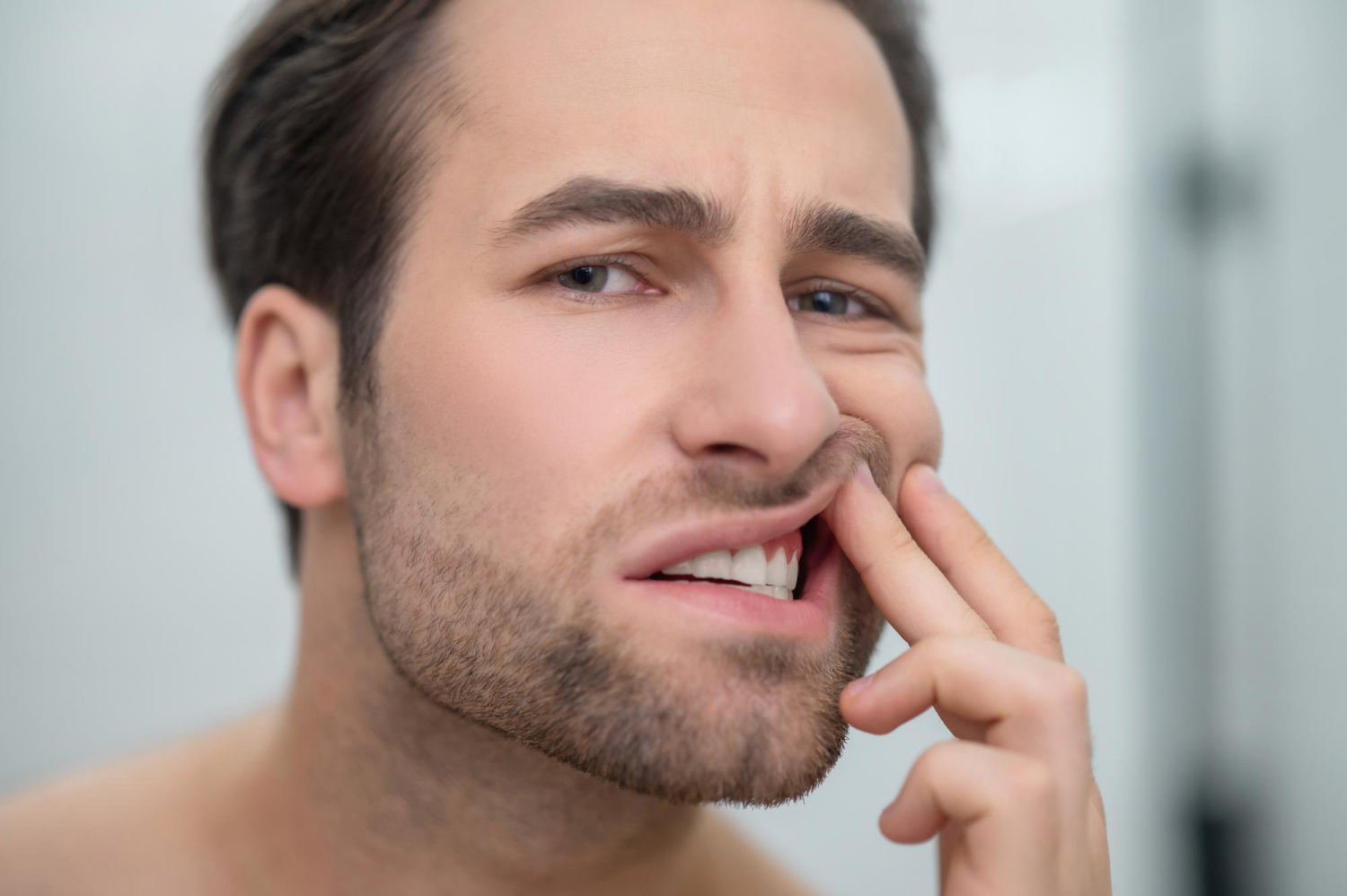 Man pulling up his upper lip and examining his teeth or gums closely with a concerned facial expression.